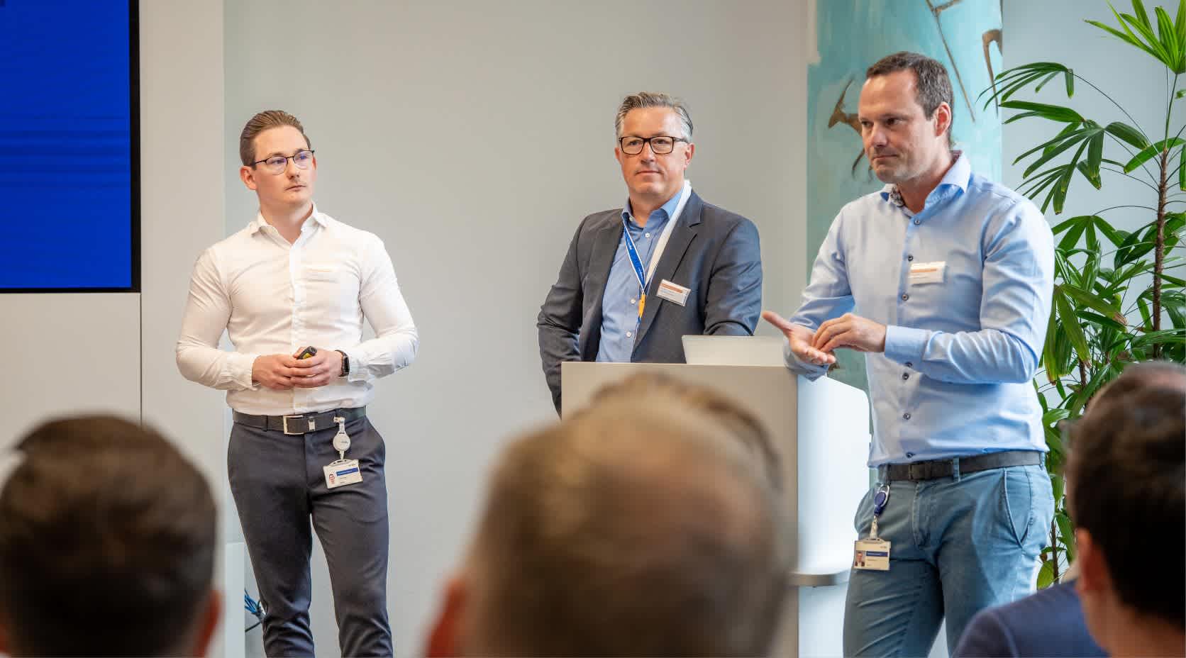 Drei Männer halten eine Präsentation vor einem Redepult