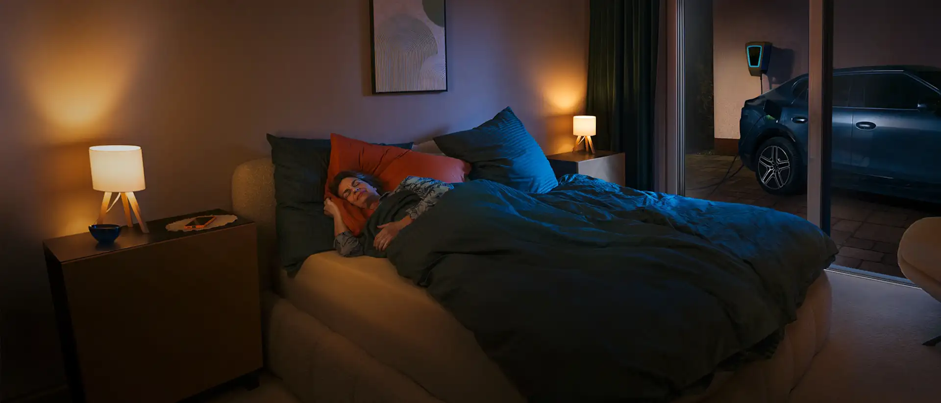 Frau schläft im Schlafzimmer, im Hintergrund lädt das Auto an einer Wallbox