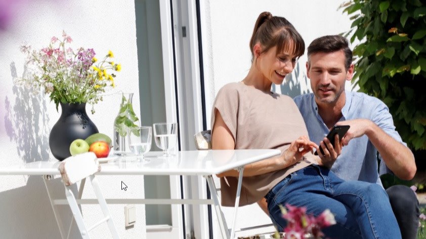 Paar auf Terrasse überprüft Stromverbrauch mit Smartphone 