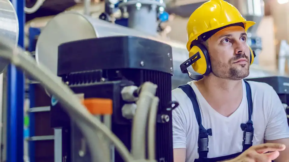 Mann mit Helm und Hörschutz im Blaumann prüft Technik im Gaskraftwerk