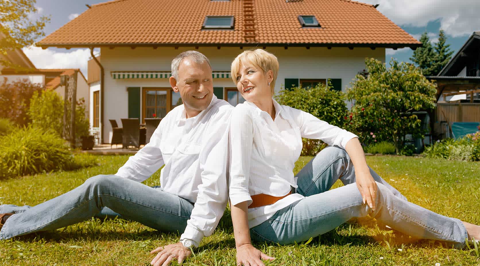 Ein älteres Ehepaar sitzt auf dem Rasen vor einem Einfamilienhaus