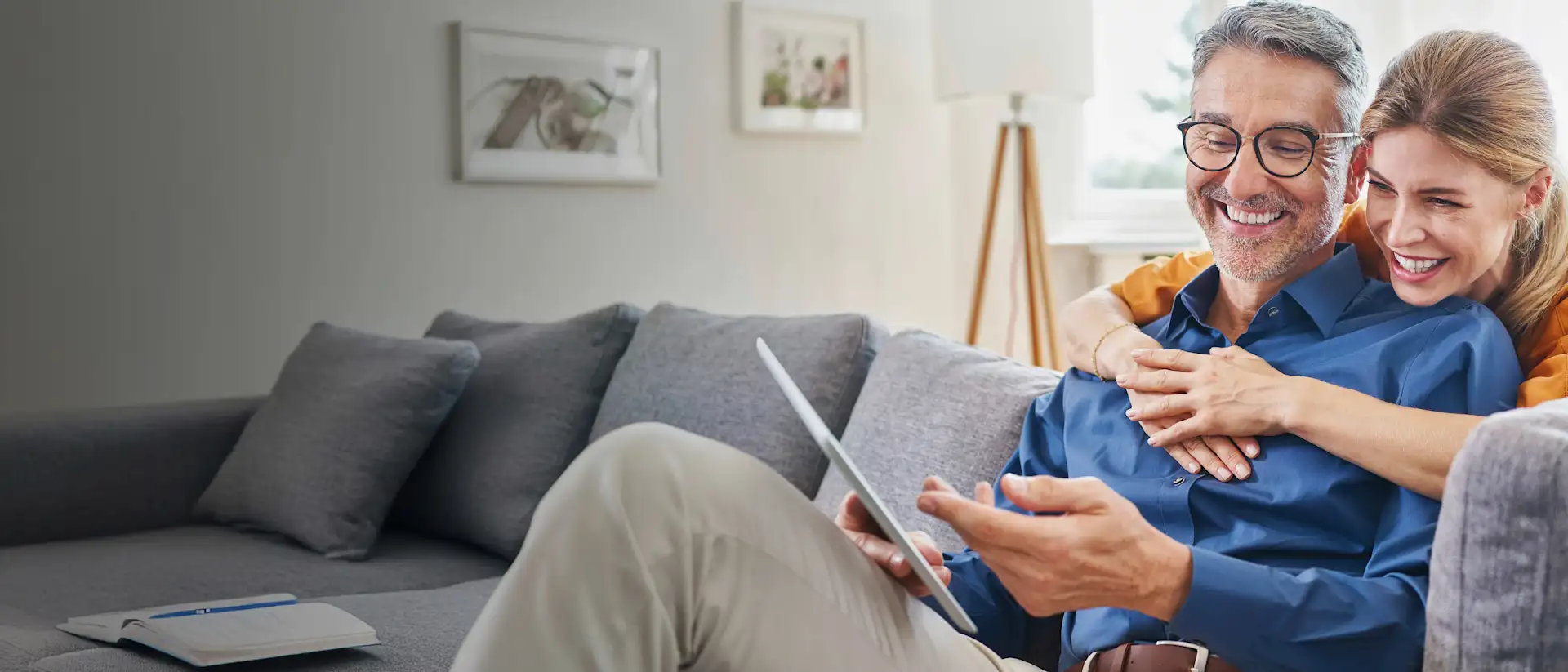 Mann und Frau sitzen lächelnd auf der Couch mit einem Tablet