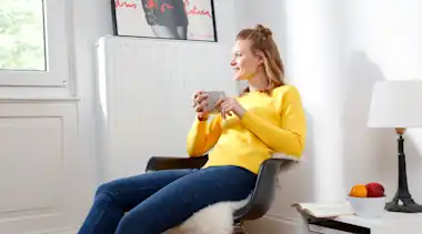 Frau mit gelbem Pullover und Tasse vor Heizung