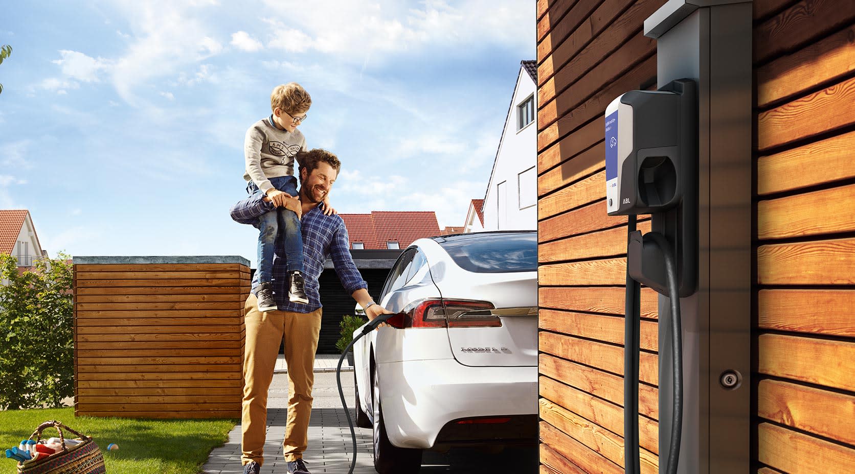 Mann mit Kind auf Schulter lädt E-Auto auf, EnBW mobility+ Wallbox im Vordergrund
