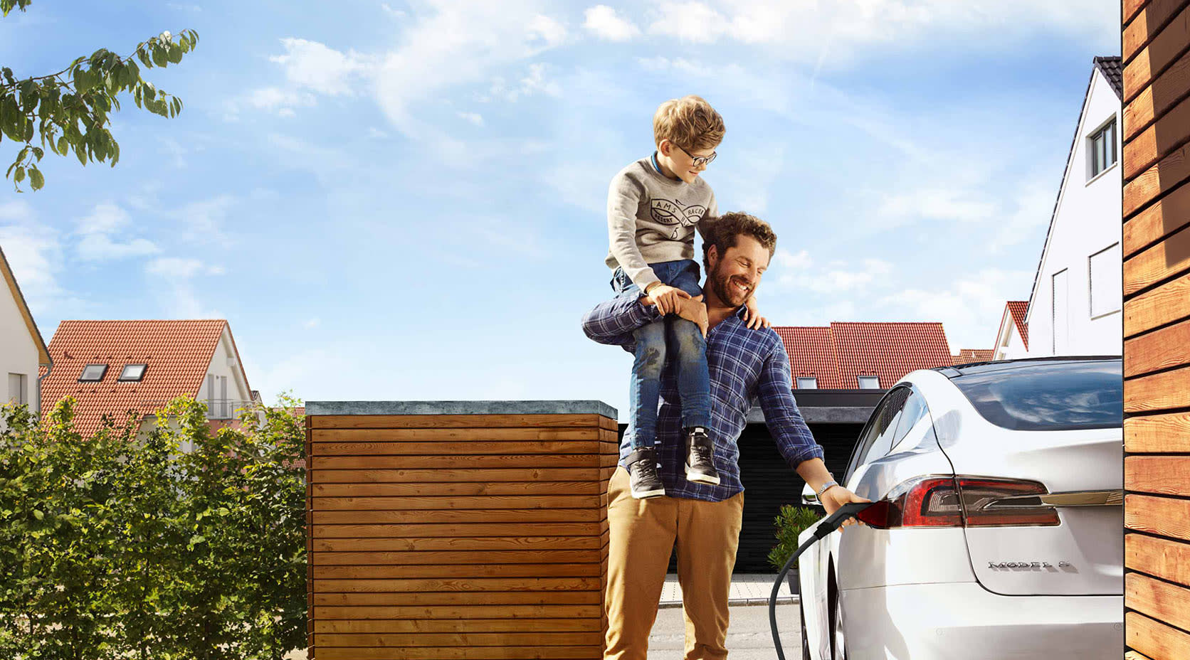 Mann mit Kind auf Schulter lädt E-Auto auf, EnBW mobility+ Wallbox im Vordergrund