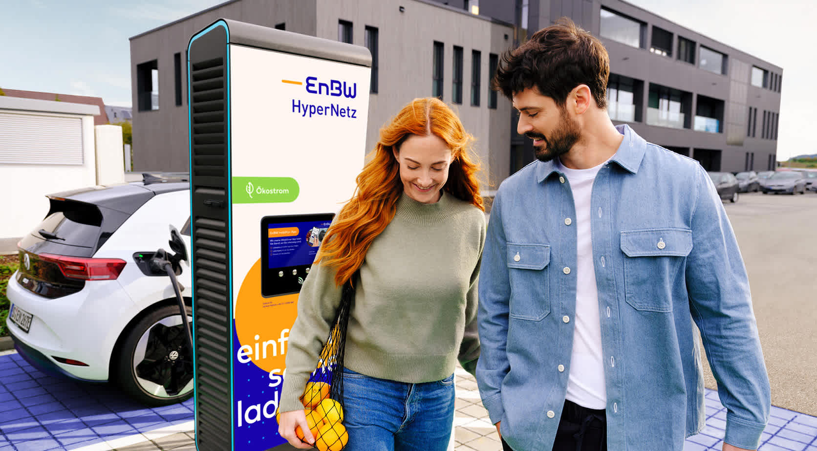 Pärchen nach dem Einkaufen auf einem Parkplatz mit EnBW Schnellladesäulen
