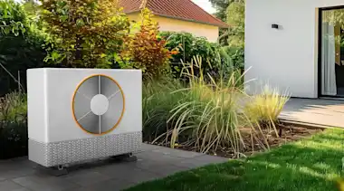 Weiße Wärmepumpe auf grüner Wiese vor Terrasse