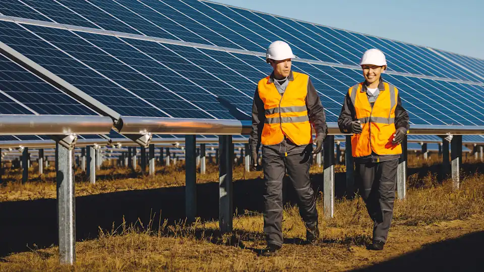Techniker und Technikerin laufen vor einer Photovoltaik-Anlage