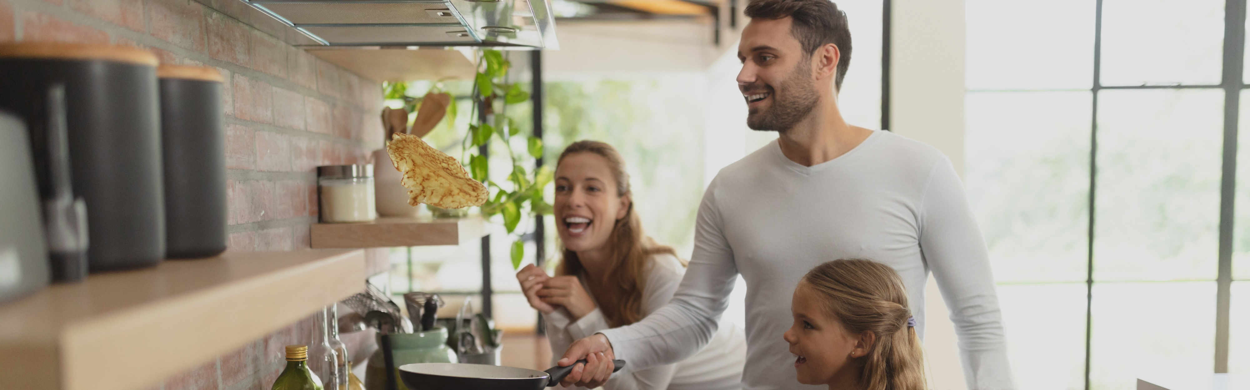 Familie backt Pfannkuchen an Gasherd. Vater wendet Pfannkuchen wie Profi.