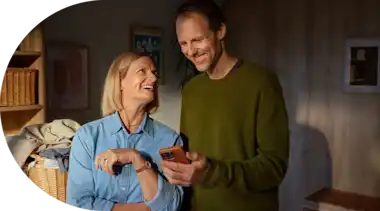 Eine Ehepaar steht in der Waschküche und schaut lächelnd auf ein Smartphone.