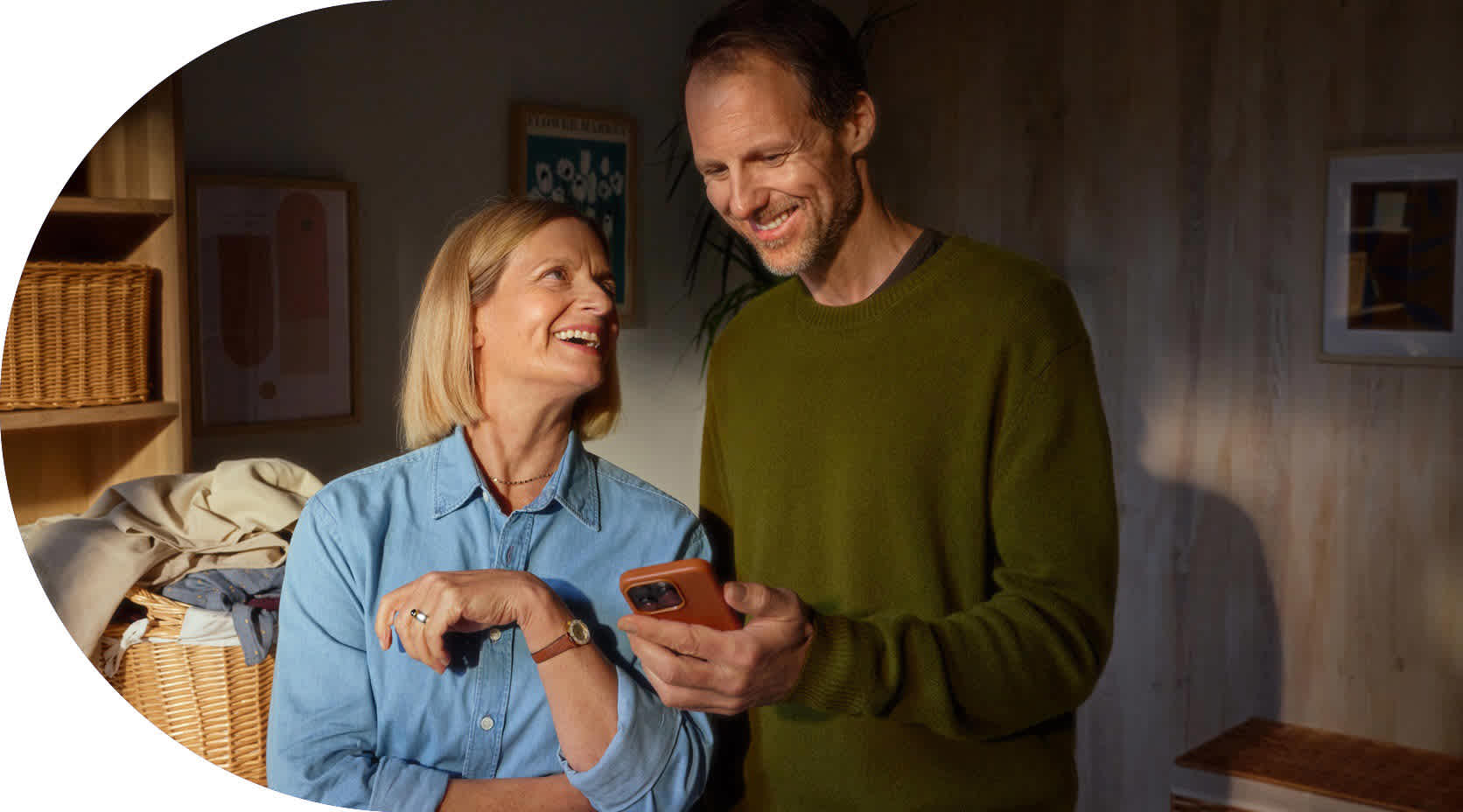 Eine Ehepaar steht in der Waschküche und schaut lächelnd auf ein Smartphone.