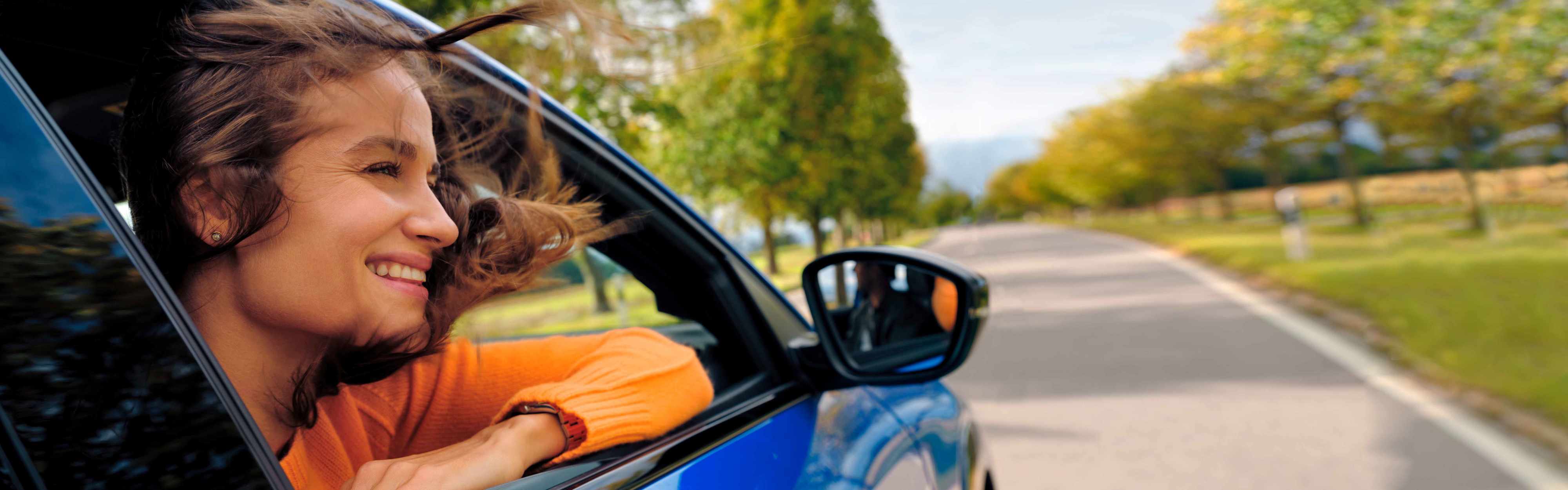 Lachende Frau schaut aus dem Fenster eines E-Autos.
