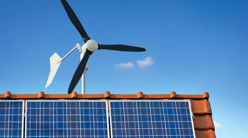 Dach mit Solaranlage und Heim-Windkraftrad zu Hause vor blauem Himmel