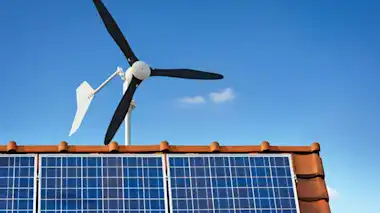 Dach mit Solaranlage und Heim-Windkraftrad zu Hause vor blauem Himmel