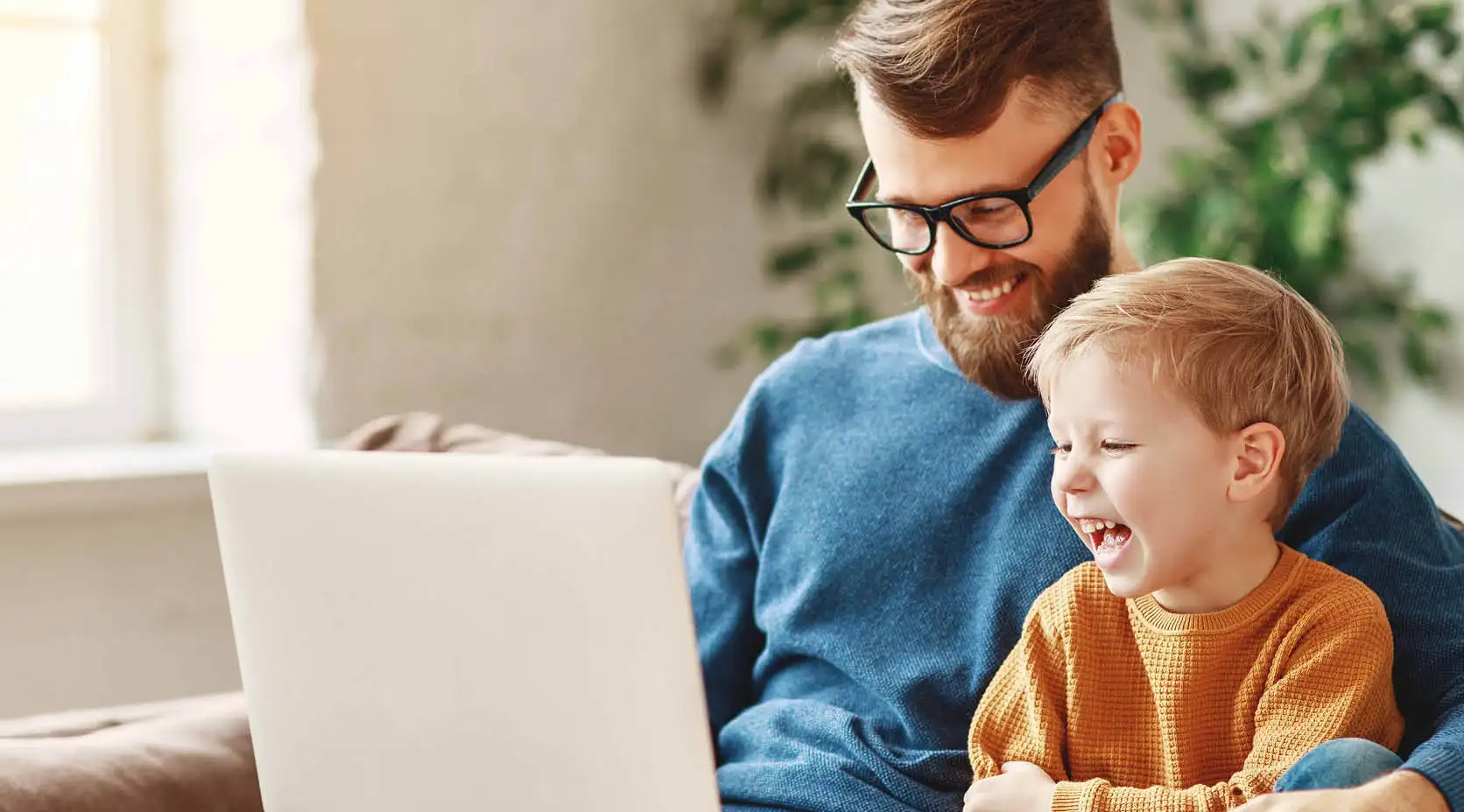 Vater und Sohn sitzen lachend mit Laptop auf dem Sofa