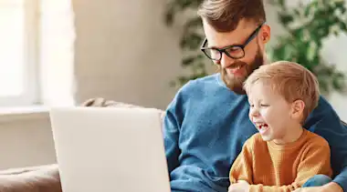 Vater und Sohn sitzen lachend mit Laptop auf dem Sofa