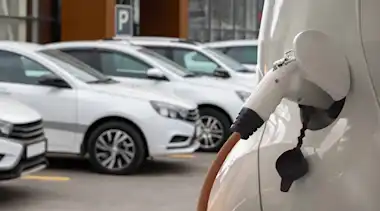 Weißes Elektroauto am Laden auf dem Parkplatz im Hintergrund sind weiße Autos