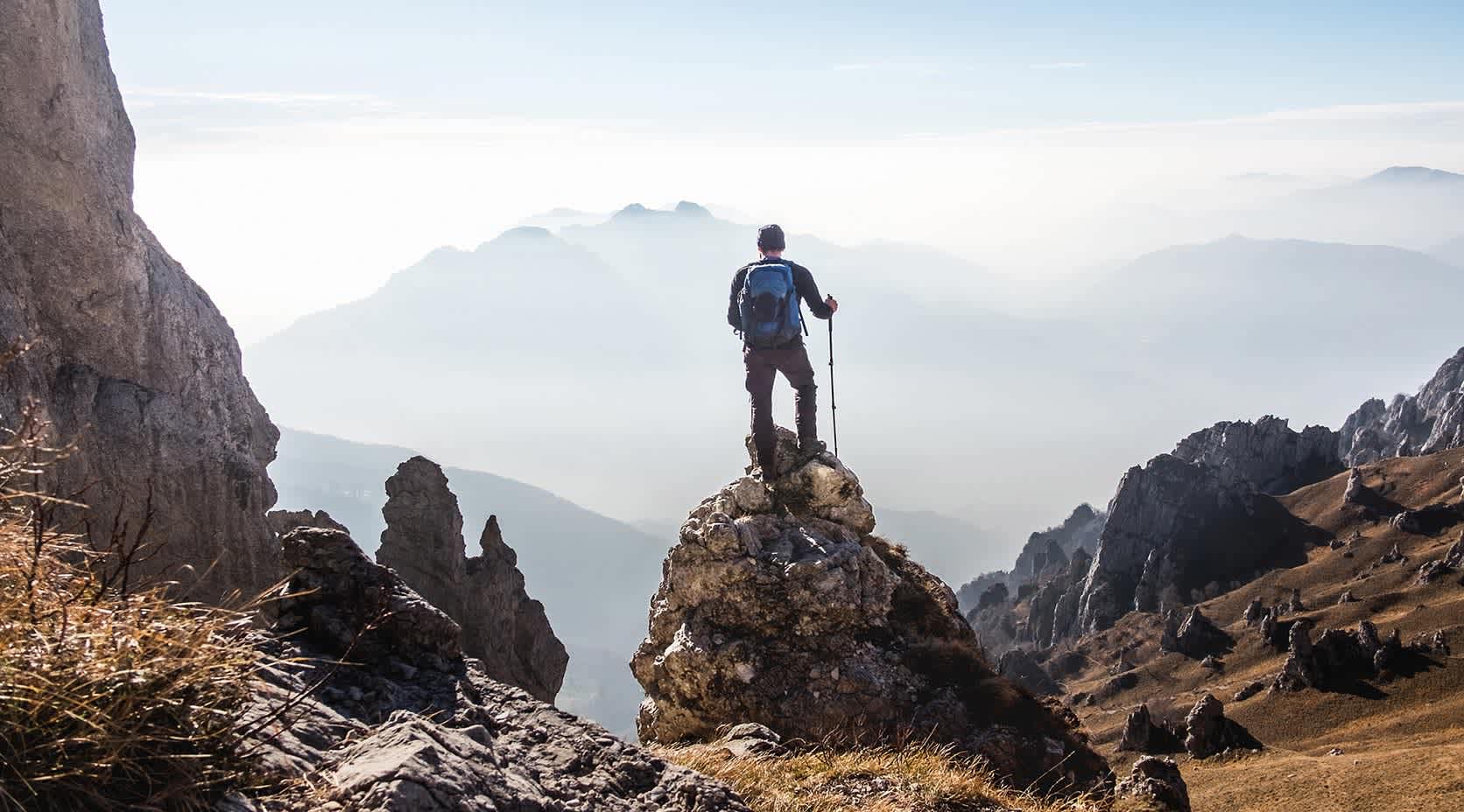 Mann mit Rucksack und Wanderstöcken auf einer Hügelspitze