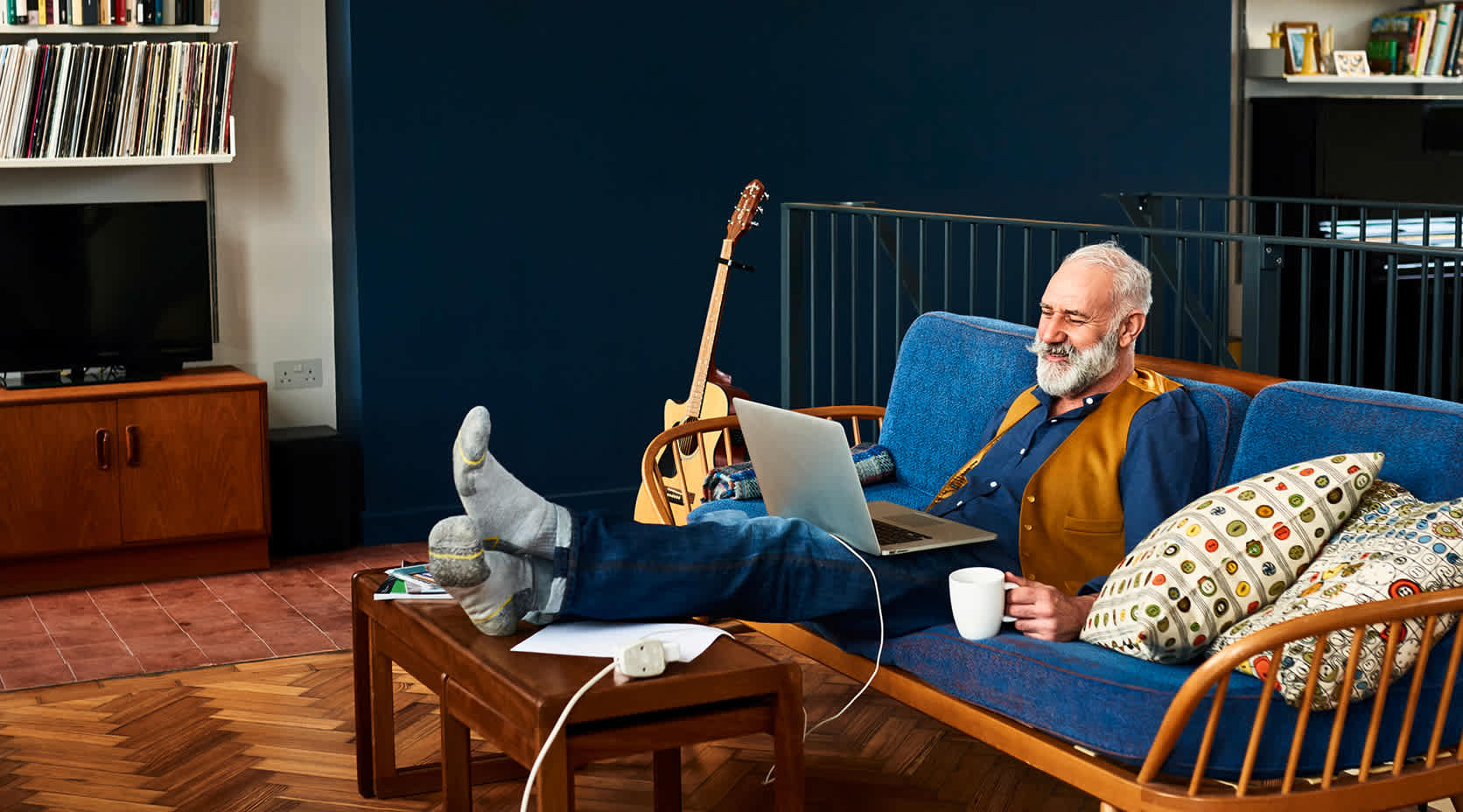 Älterer Mann auf der Couch mit Laptop auf den Beinen.

