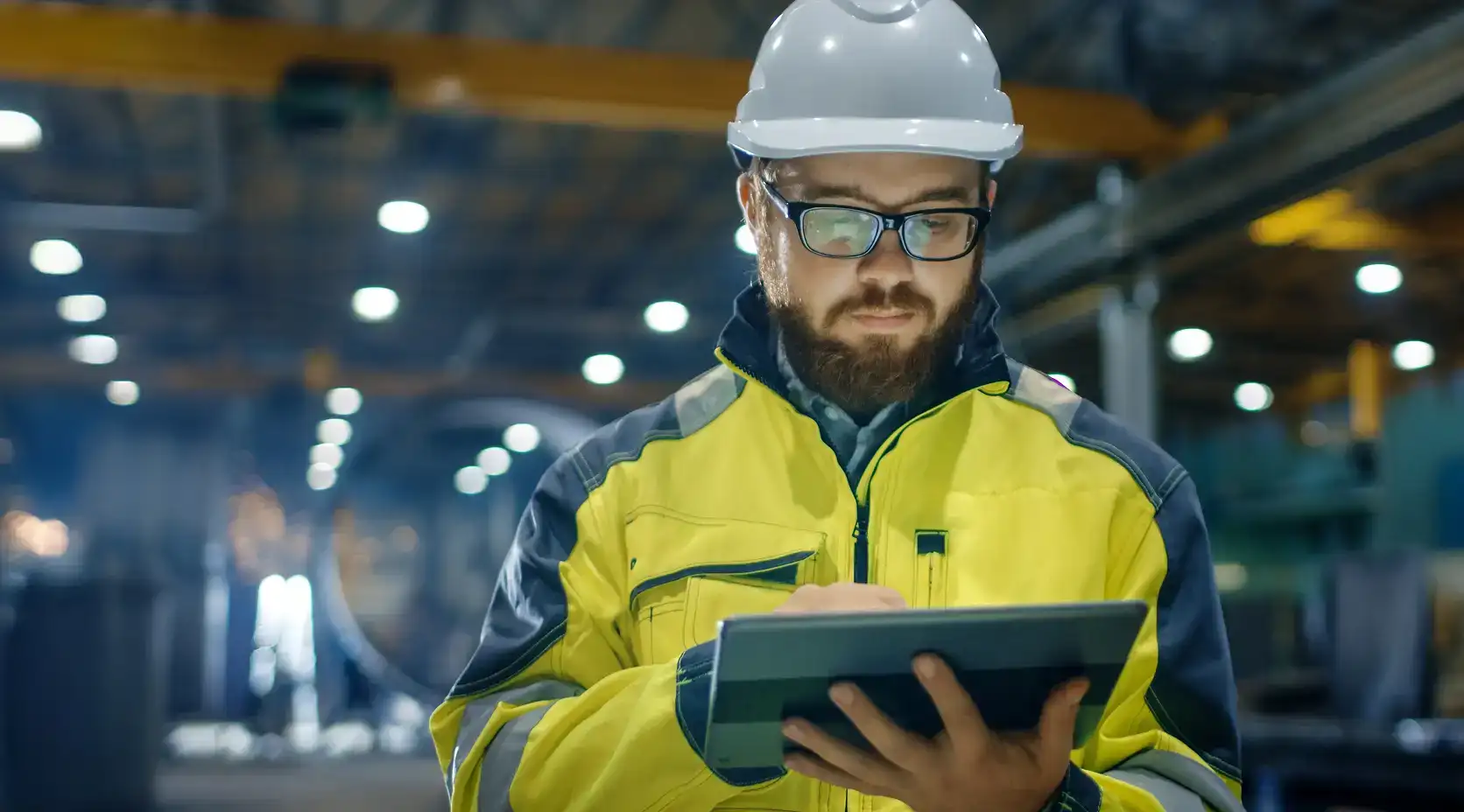 Mann mit Tablet steht in einer Lagerhalle, er trägt Schutzhelm und Schutzkleidung