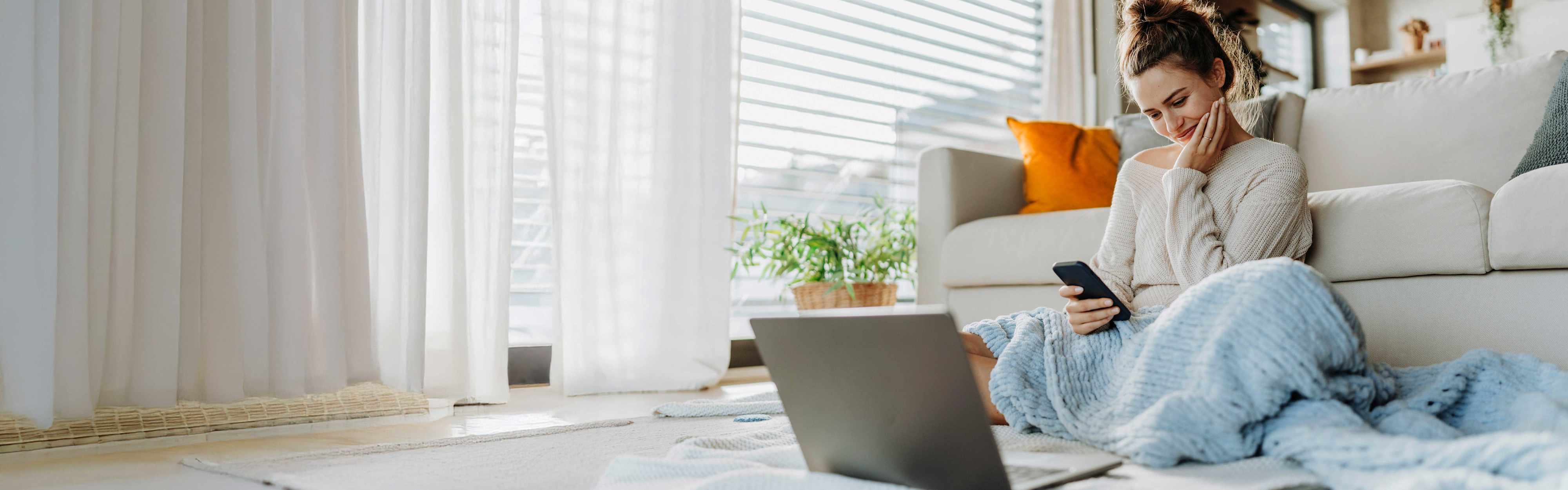 Junge Frau mit Handy vor dem Sofa.