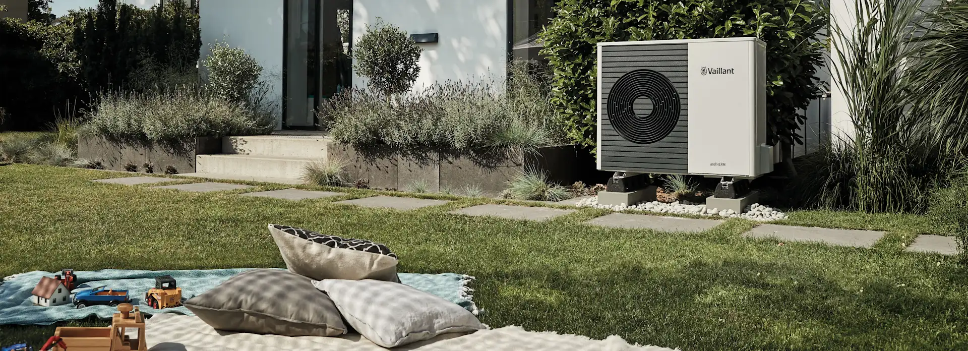 Decken und Spielzeug in einem Garten mit einer Wärmepumpe im Hintergrund.