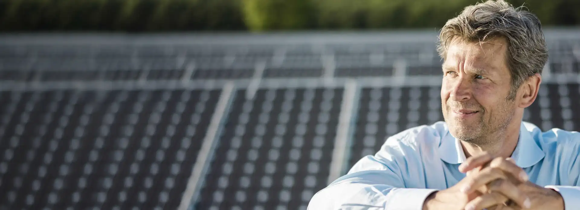 Grauhaariger Mann steht in einer PV/Solaranlage zwischen Solarpanel