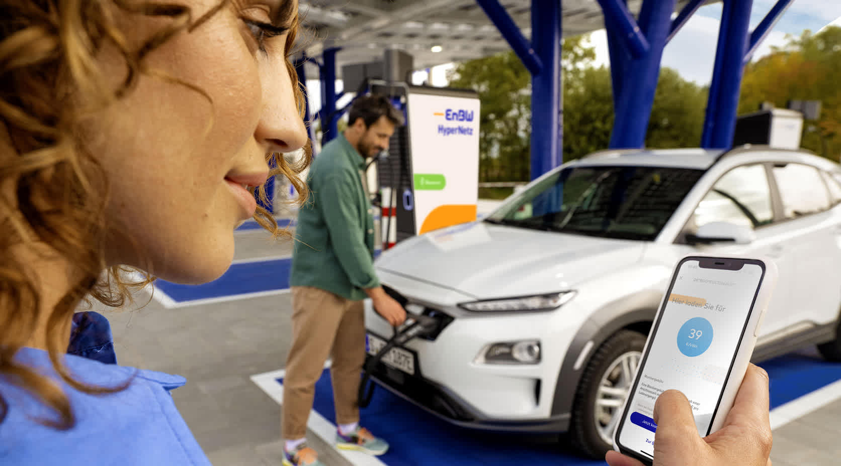 Frau an Ladesäule und schaut auf das Smartphone