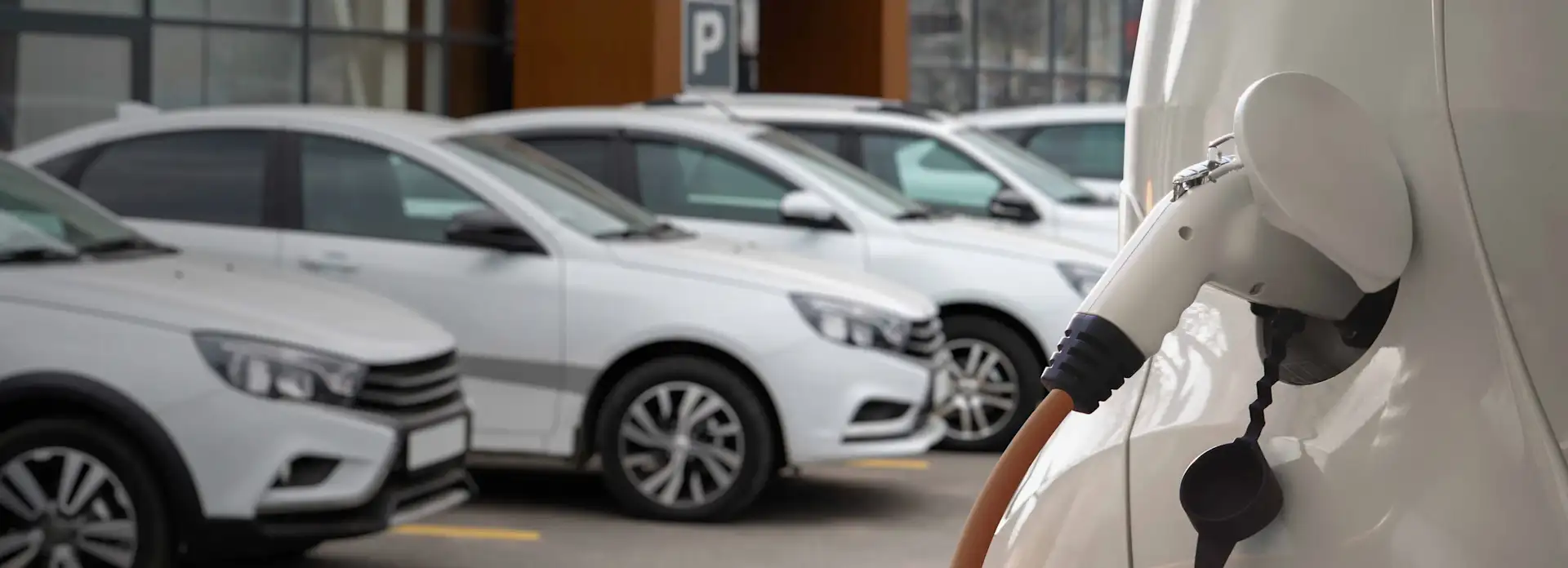 Weißes Elektroauto am Laden auf dem Parkplatz im Hintergrund sind weiße Autos