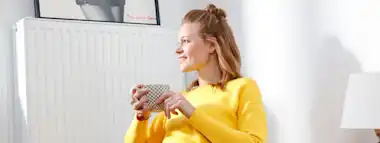 Zufriedene Frau sitzt vor Heizung