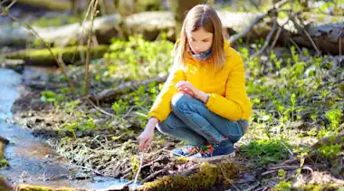 Mädchen in gelber Jacke spielt im Wald am Fluss Stock