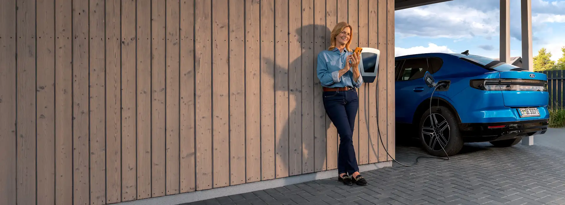 EnBW Frau Ladestation Elektroauto Wallbox Carport Smartphone Mavi Ladeübersicht