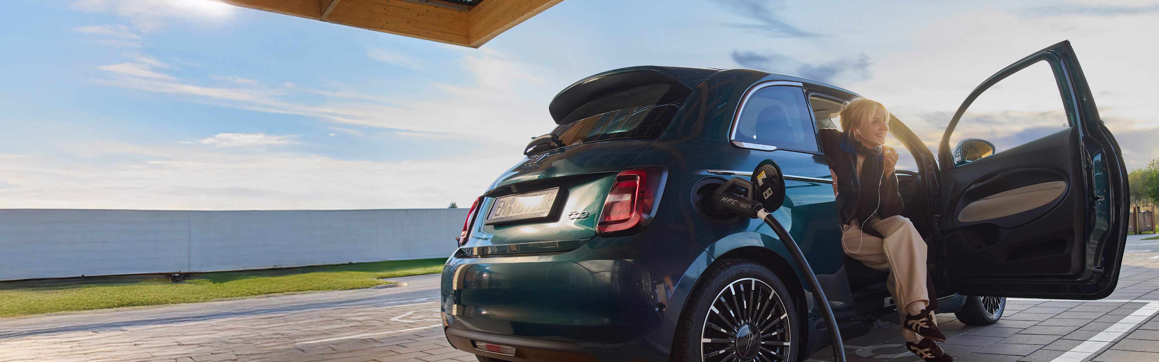 Eine junge Frau lädt während des Sonnenuntergangs ihr Elektroauto an einer EnBW Ladesäule.