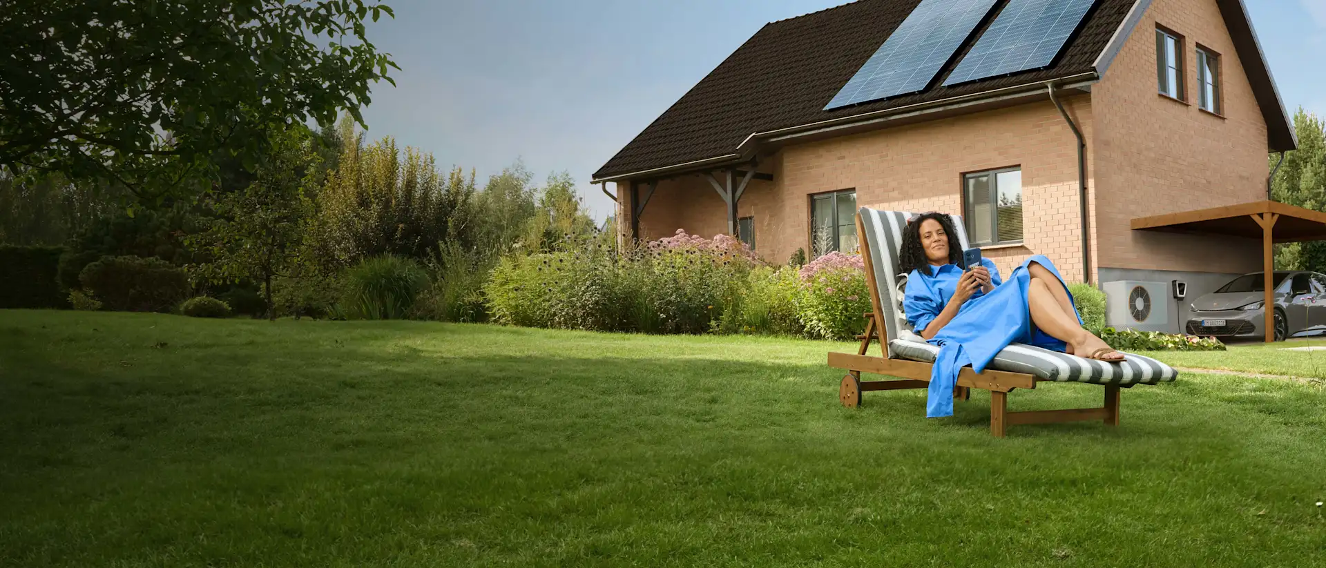 Eine Frau liegt entspannt auf einem Liegestuhl im Garten ihres Hauses.