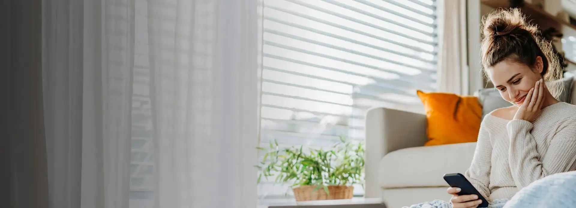 Junge Frau mit Handy vor dem Sofa.