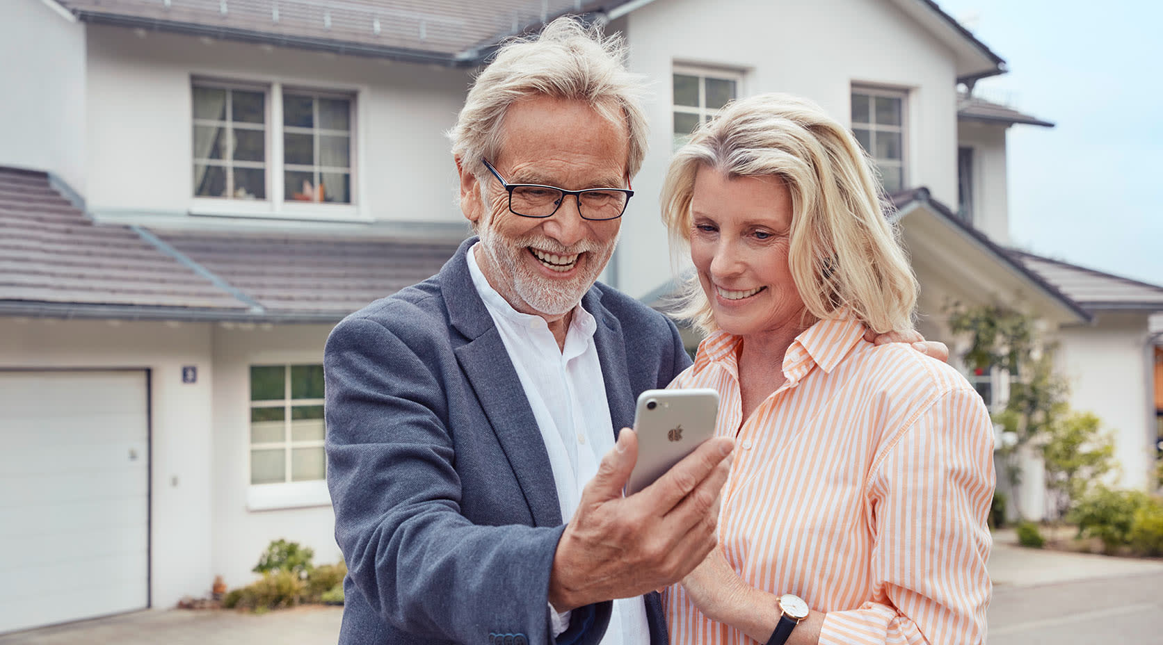 Älteres Paar mit Smartphone vor Eigenheim