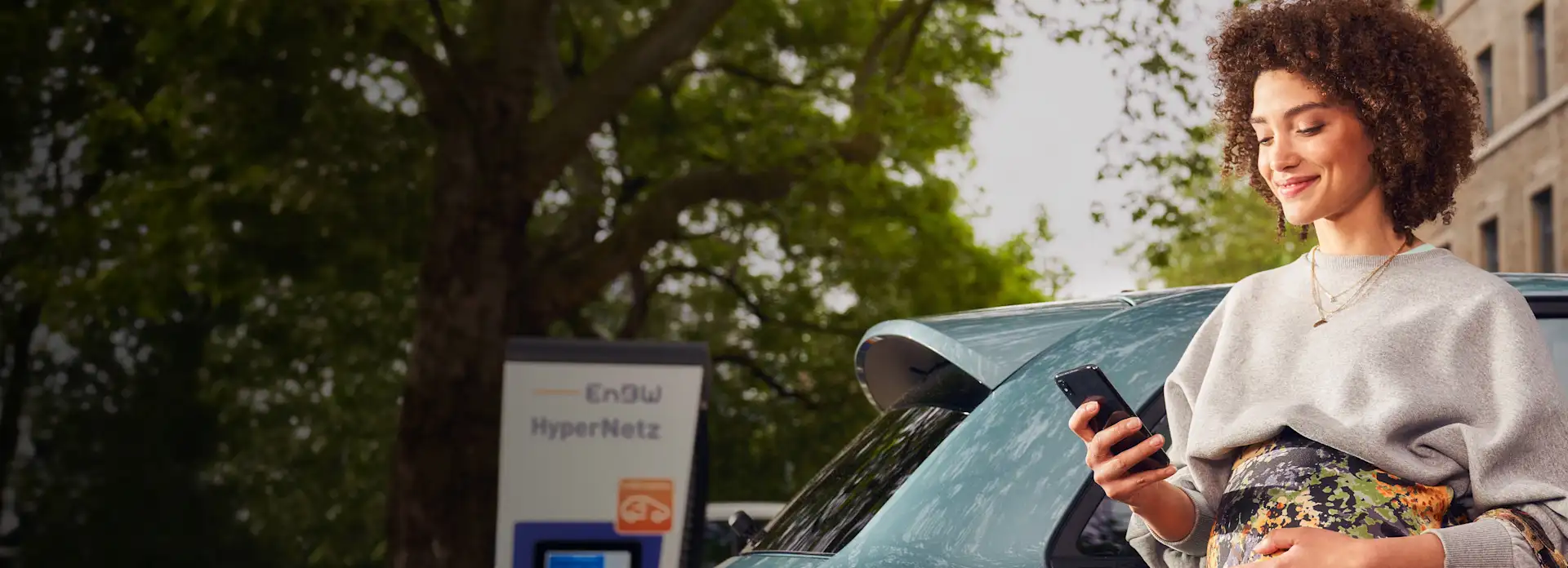 Schwanger Frau Smartphone E-Auto Ladesäule Elektromobilität