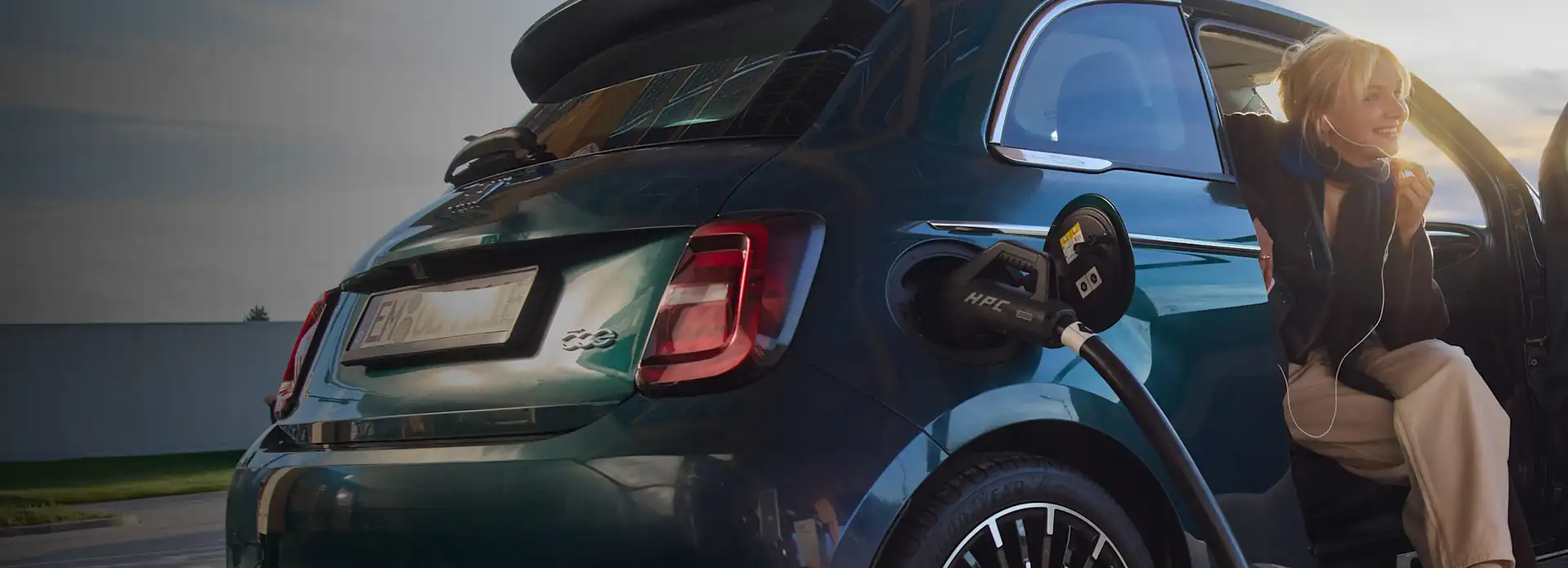 Eine junge Frau lädt während des Sonnenuntergangs ihr Elektroauto an einer EnBW Ladesäule.