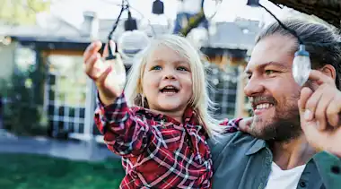 Vater hält Tochter im Arm und zeigt ihr eine Lichterkette am Baum