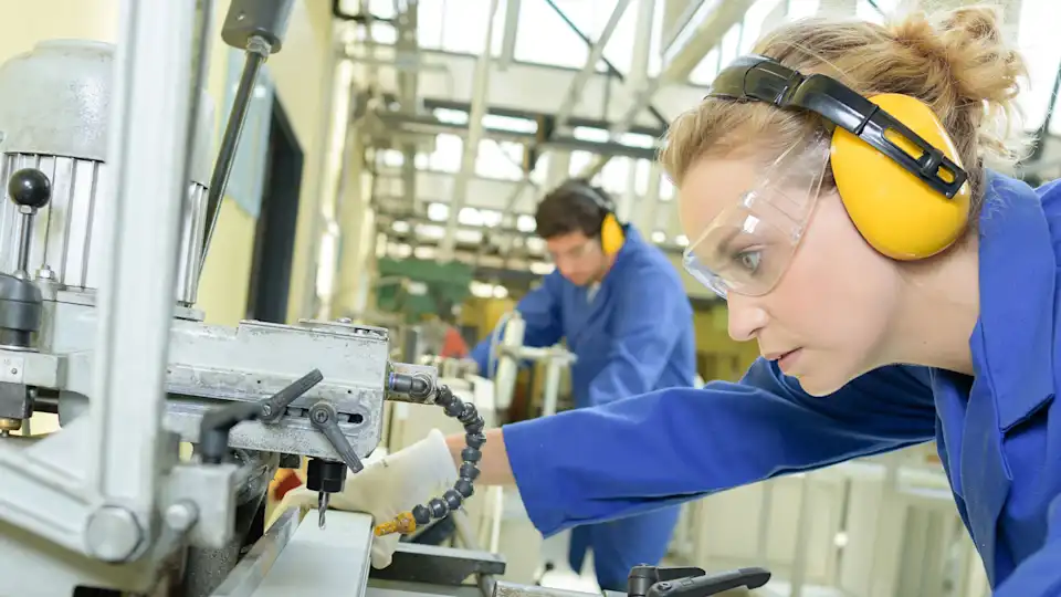 Frau mit Hörschutz und Brille an Betriebsmaschine in der Maschinenhalle