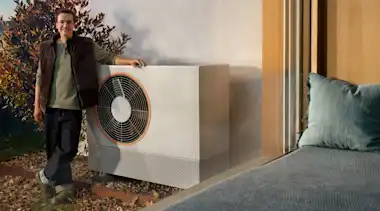 Ein Mann steht im Garten und lehnt sich an seine Wärmepumpe an.