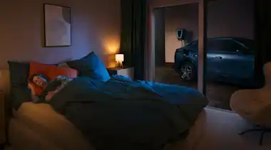 Frau schläft im Schlafzimmer, im Hintergrund lädt das Auto an einer Wallbox