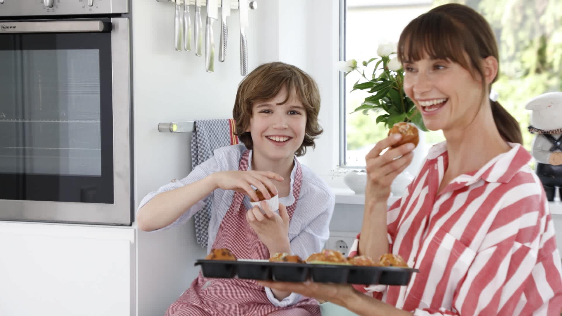 Frau und Kind sind in der Küche und probieren Muffins