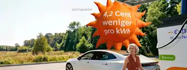 Frau lädt E-Auto an EnBW-Ladestation im EnBW HyperNetz, hinter ihr schwebt ein Luftballon in Form einer Sonne mit der Aufschrift "4,2 Cent weniger pro KWh"