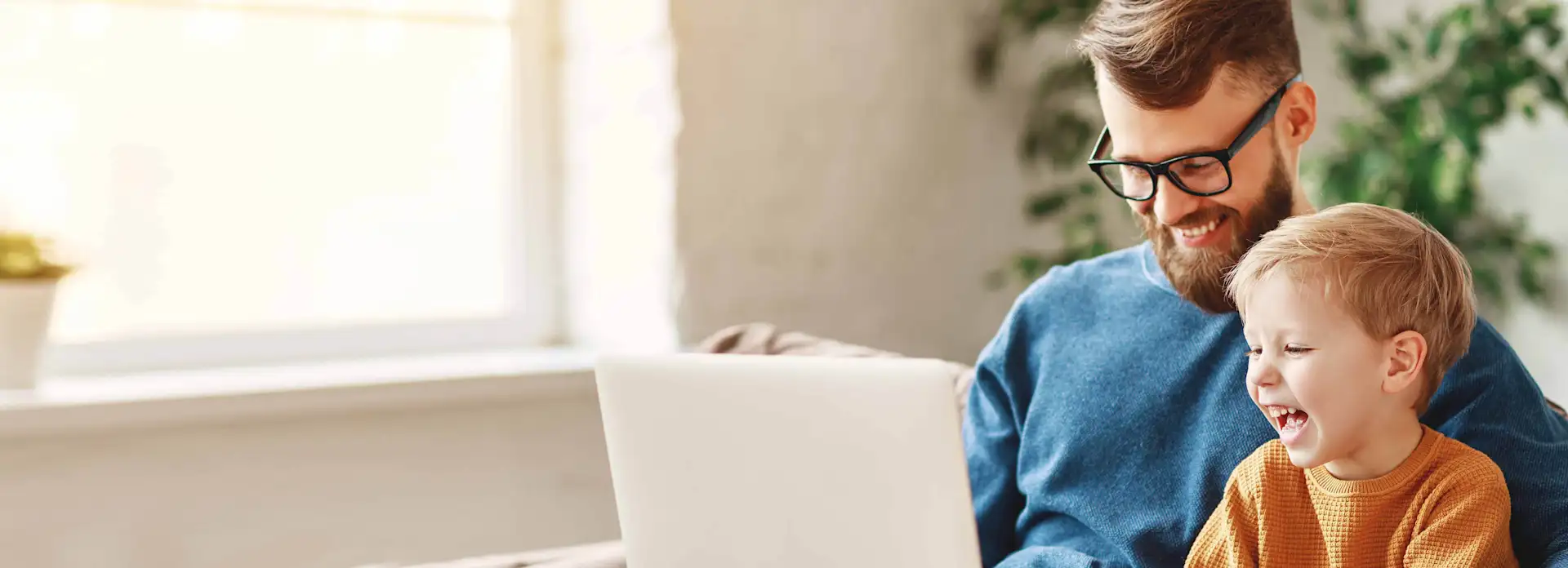 Vater und Sohn sitzen lachend mit Laptop auf dem Sofa