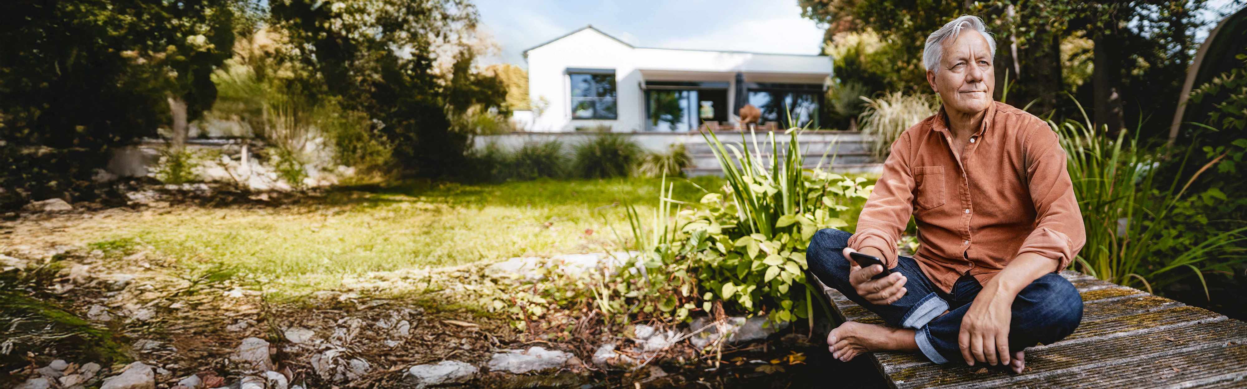 Mann mit Smartphone sitzt im Garten an einem Teich