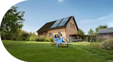 Eine Frau liegt entspannt auf einem Liegestuhl im Garten ihres Hauses.