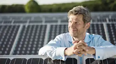 Grauhaariger Mann steht in einer PV/Solaranlage zwischen Solarpanel