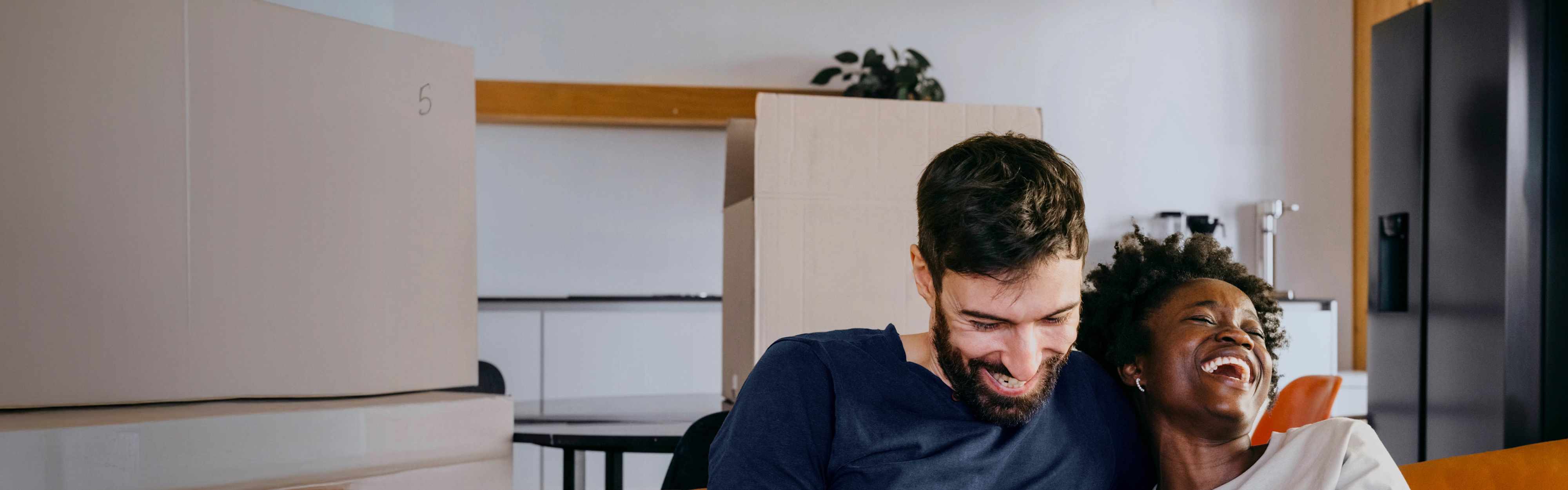 Ein junges Pärchen sitzt lachend auf der Couch und schaut auf ein Smartphone.