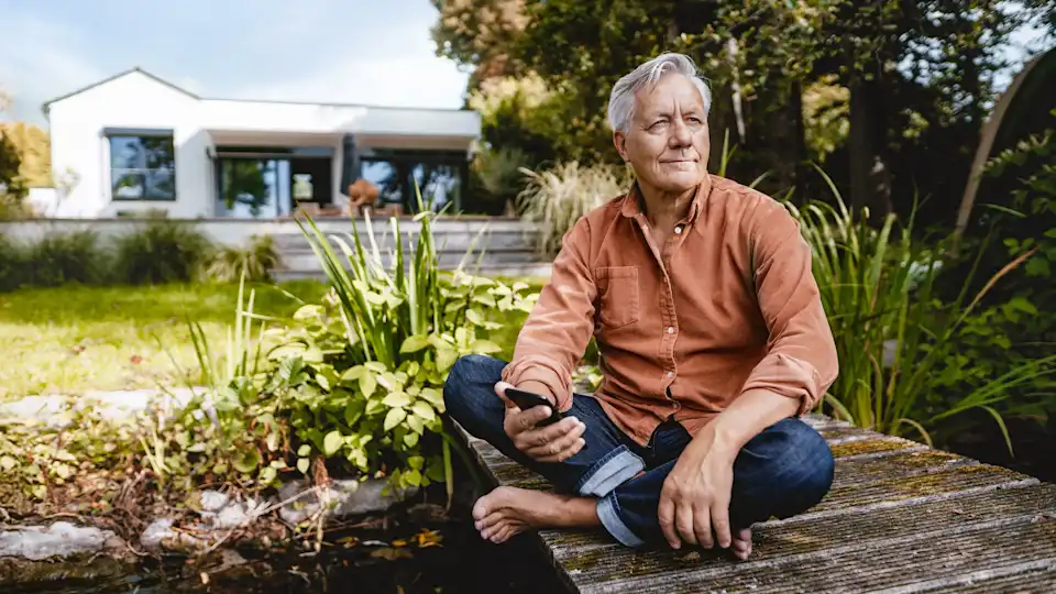 Mann mit Smartphone sitzt im Garten an einem Teich